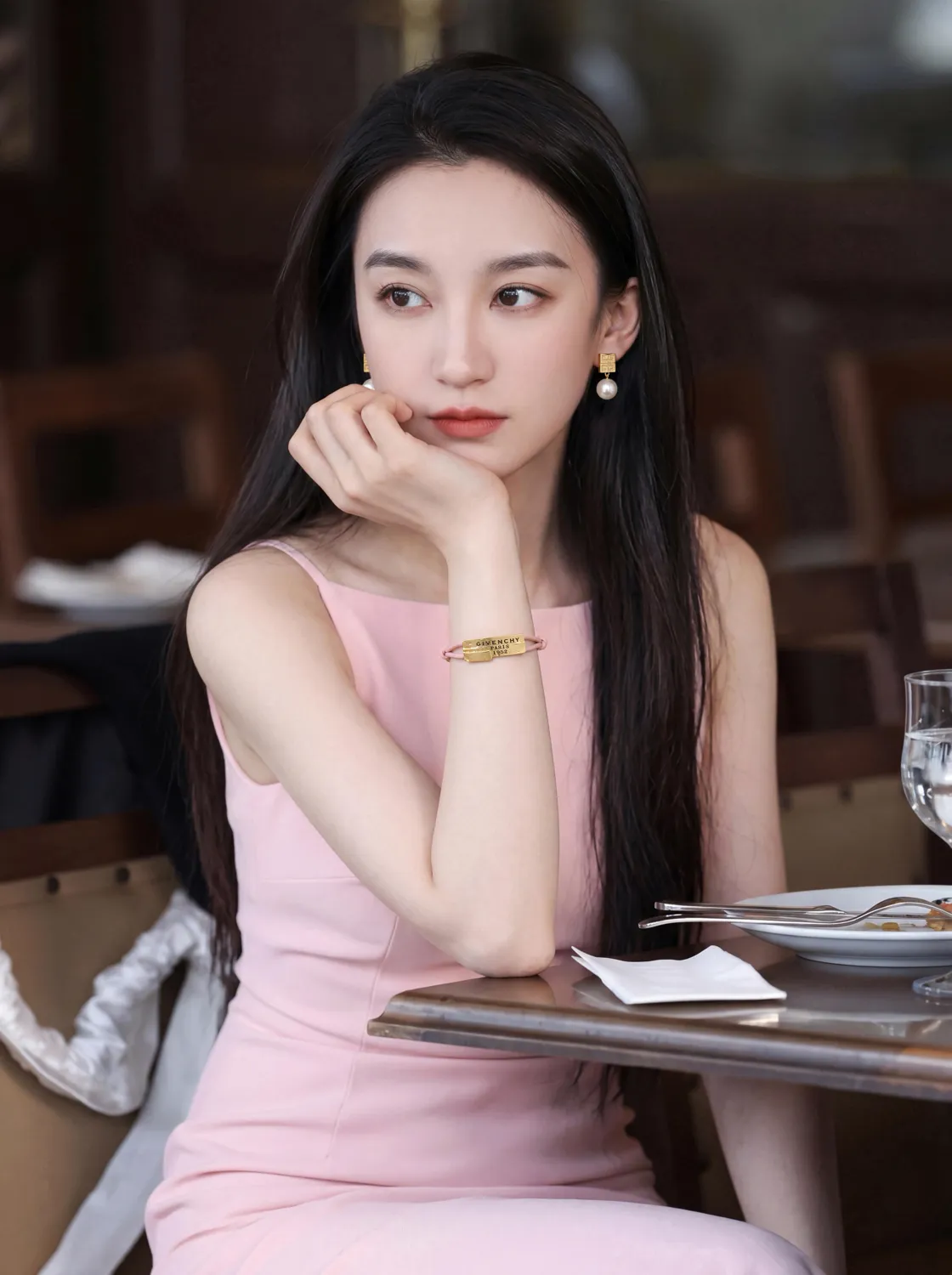 Model in a pink dress wearing a gold bracelet at a café